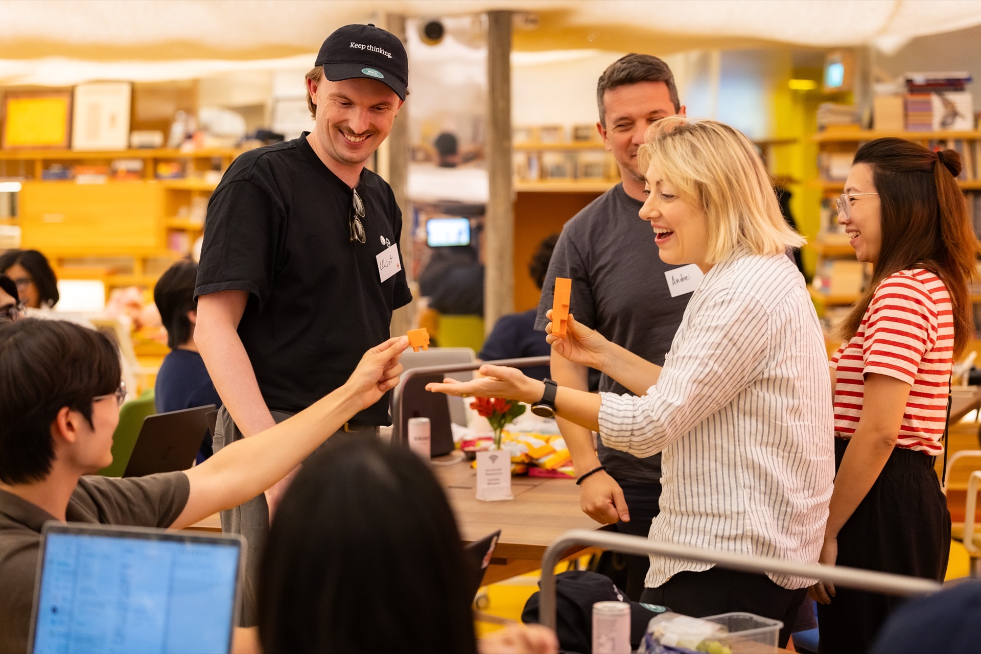 Elliot smiling with a group as they compare rough orange block prototypes around a table